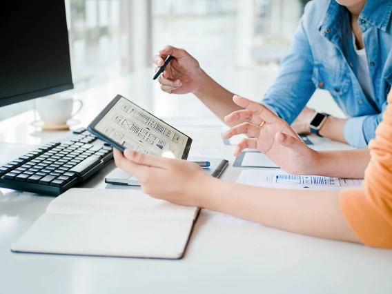 Close up shot of two people at a desk looking at graphical figures on a tablet