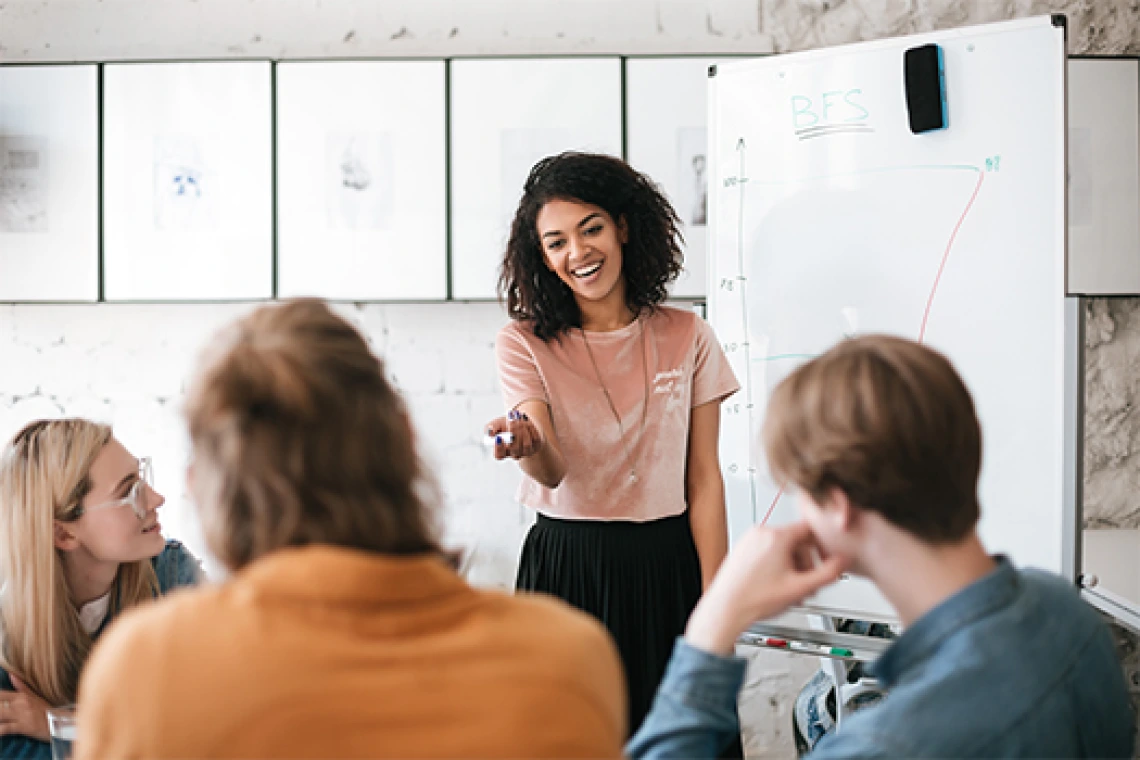 Smiling student talks to a small group of peers in a classroom setting