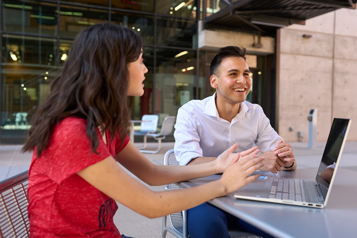 Two students sitting outside on a laptop having a conversation