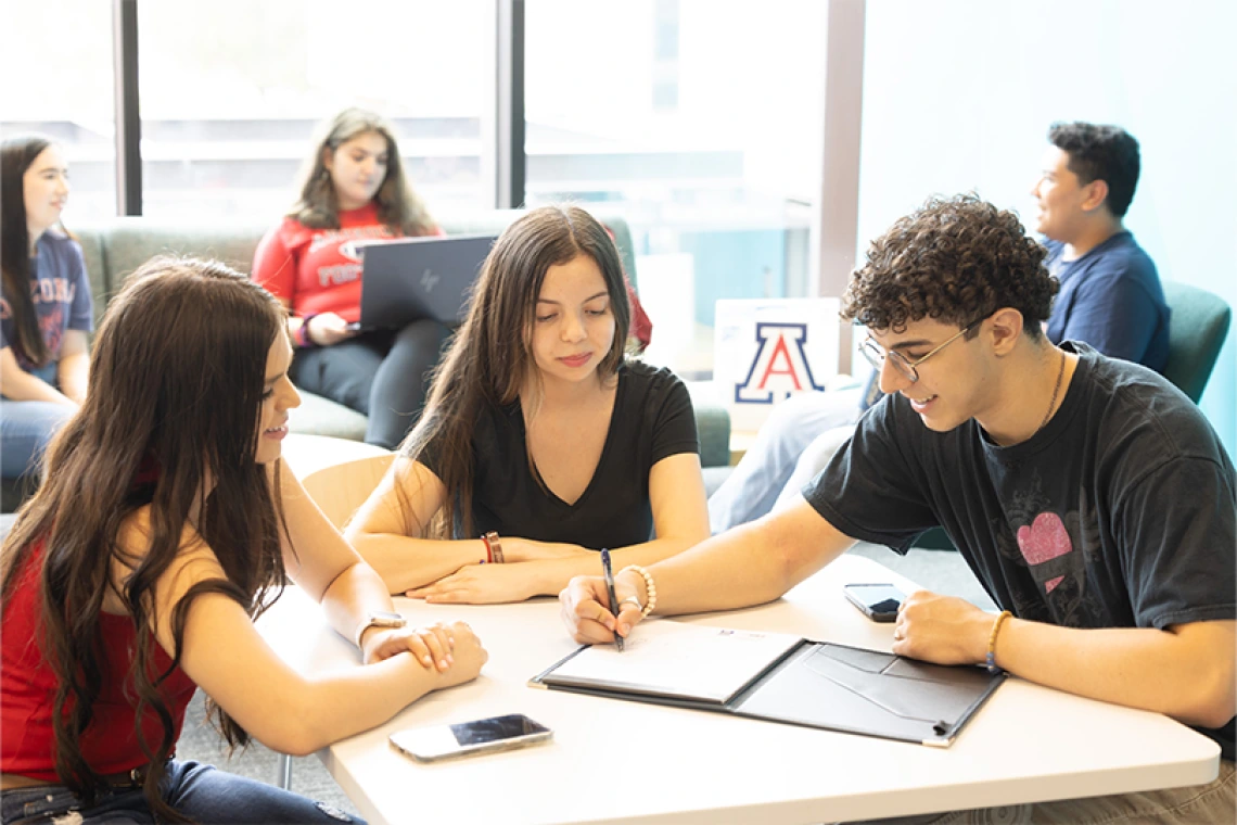 Group of students sitting inside at a table working on schoolwork