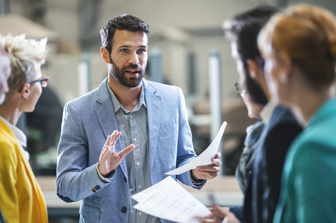 Man holding papers speaking to a group of professionals