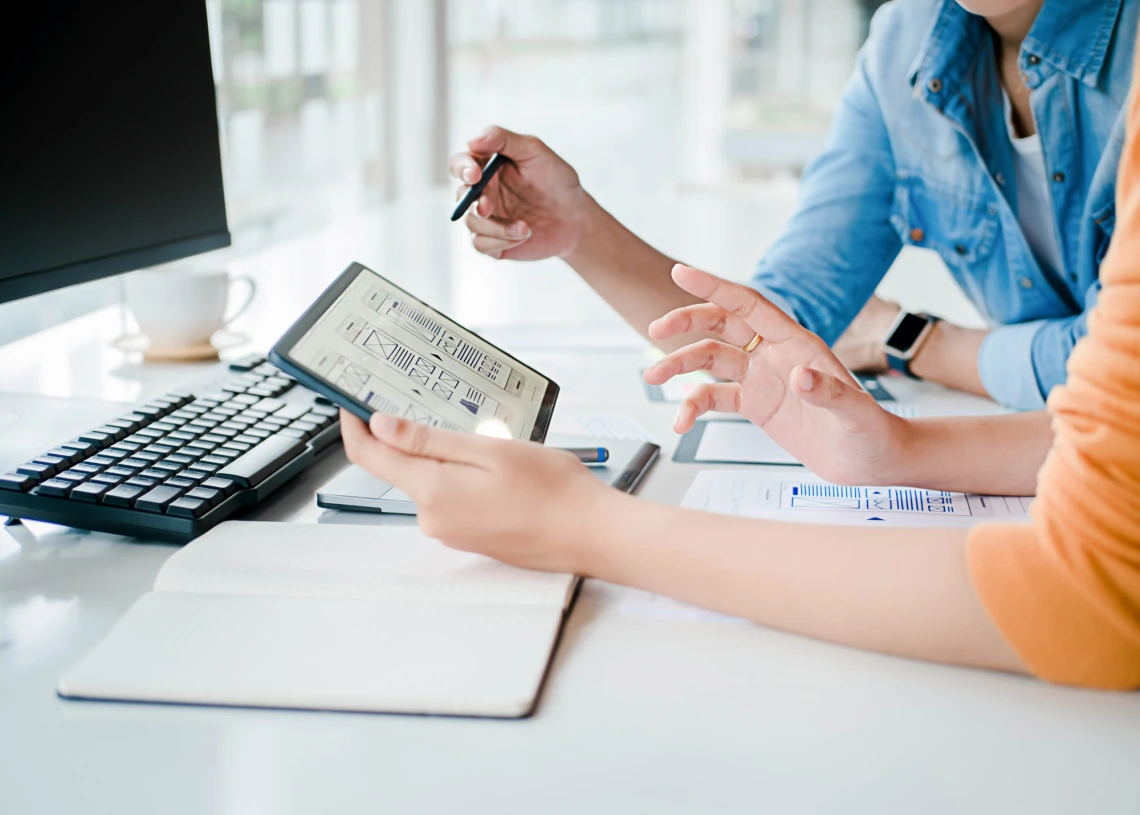 Close up shot of two people at a desk looking at graphical figures on a tablet